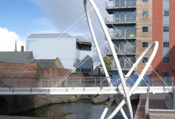 A white architectural footbridge in an urban town center area. 